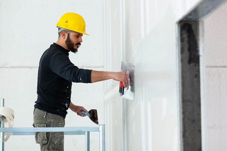 Drywall Contractor Insurance - Drywall Worker in Yellow Helmet Plastering Wall While Standing on Scaffold