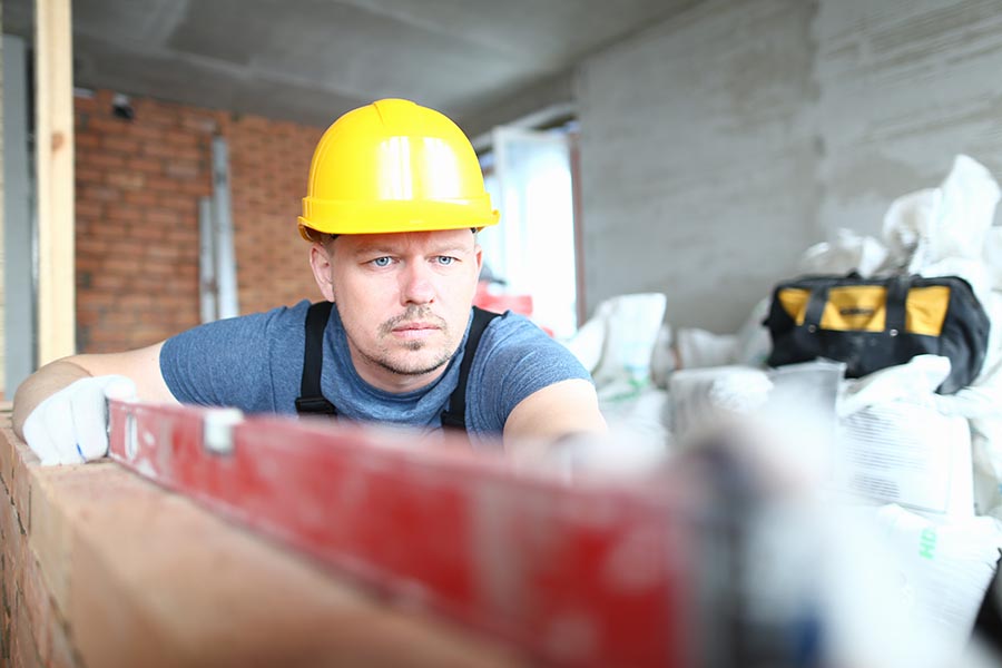Specialized Business Insurance - Contractor Uses a Level on a Job, Wearing a Yellow Hard Hat